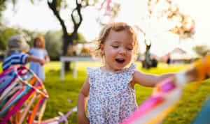 一個微笑的幼兒女孩在陽光明媚的公園裡玩彩色飄帶。 — 柏林 壁紙