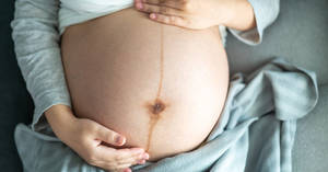 一位孕婦的肚子被她的雙手托在柔軟的灰色布料上。 — 懷孕 壁紙