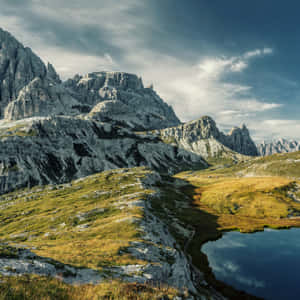 高聳的岩石山脈，有草地斜坡和反射天空的湖泊。 — 自然 iPhone 壁紙