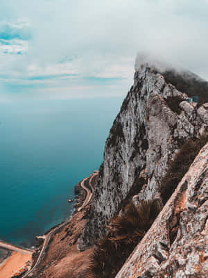 陡峭的懸崖，沿海岸有一條蜿蜒的道路，在陰天之下俯瞰海洋。 — 岩石 壁紙
