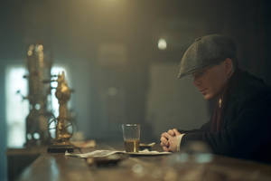 戴平頂帽的男人坐在酒吧，拿著啤酒杯，在昏暗的金色光線中 — 湯瑪斯·謝爾比 壁紙