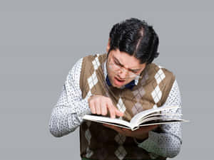 戴眼鏡和菱形花紋背心的男人，震驚地指著一本書。 — 宅男 壁紙