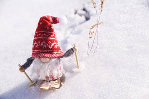 節日地精戴紅帽踩滑雪板坐在雪地，附近有乾草。 — 可愛聖誕節 壁紙