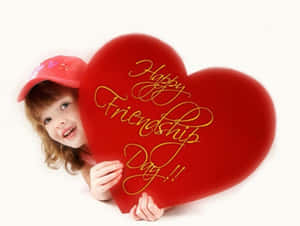 小孩拿著一個紅心，上面用金色寫著「Happy Friendship Day」。 — 慶祝 壁紙