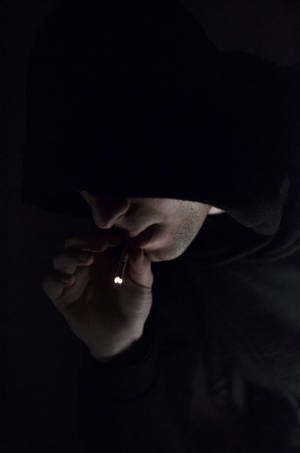 一個穿著深色連帽衫的人在昏暗光線下用火柴點燃香煙。 — 抽菸 壁紙