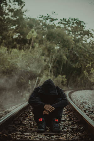 一個穿著黑色連帽衫的人獨自坐在霧氣森林中的火車軌道上。 — 獨自一人 壁紙