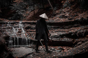 一個戴著圓錐形帽子的人，在森林的瀑布附近拿著一把劍。 — 混沌武士 壁紙