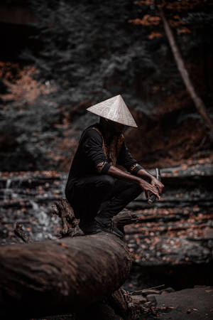 戴圓錐形帽子的人蹲在森林小溪旁的木頭上 — 混沌武士 壁紙