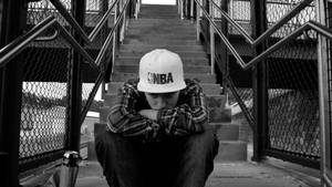 一個戴著白色NBA帽的年輕男子沮喪地坐在混凝土樓梯上。