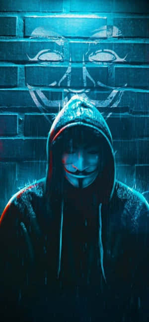 穿連帽衫和戴蓋伊·福克斯面具的人站在雨中，背景是磚牆和塗鴉面具。 — iPhone 15 壁紙