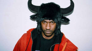 戴著黑色牛角帽和紅色外套的男人直視鏡頭。 — Skepta 壁紙