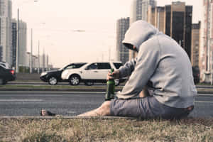 一個穿連帽衫的人坐在路邊，手持啤酒瓶，汽車駛過。 — 痛苦語錄 壁紙