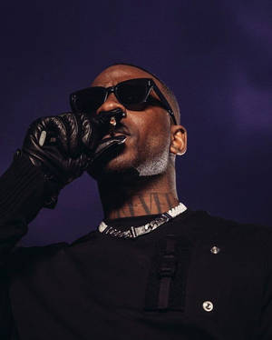 戴黑色太陽眼鏡和手套的男人在紫色背景前抽大麻煙。 — Skepta 壁紙