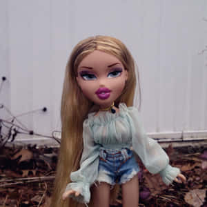 穿著網眼上衣和牛仔短褲的 Bratz 公仔，站在白色籬笆附近的落葉中。 — 娃娃 壁紙