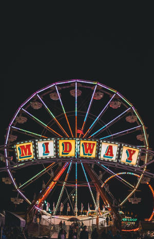 摩天輪在夜晚於遊樂園中帶有「MIDWAY」標誌發光。 — 紅魔平板 壁紙