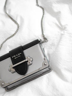 銀色Prada手提包配黑色肩帶，置於白色布料上。 — Prada 壁紙