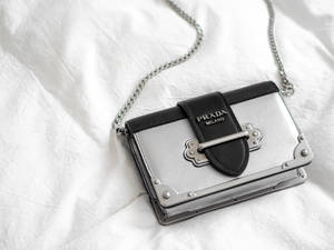 銀色和黑色Prada手提包，帶鏈條肩帶，放在白色布料上。 — Prada 壁紙