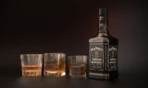 三個加冰的威士忌杯，旁邊是Jack Daniel's酒瓶，放在深色表面上。 — 昏暗 壁紙