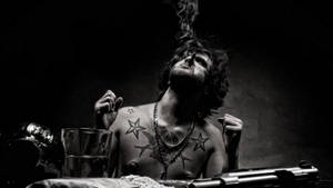 一個有刺青的男人在黑暗環境中吸煙，附近有一把槍。 — 刺青 壁紙