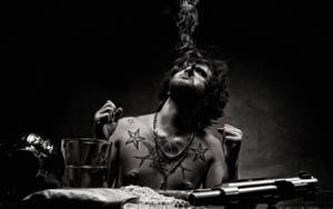 有刺青的男人在黑暗房間抽煙斗，桌上放著槍和玻璃杯。 — 美少年動態圖 壁紙