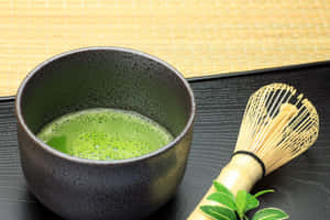 陶瓷碗中的抹茶，配以竹筅和新鮮茶葉，置於黑色托盤上。 — 茶 壁紙