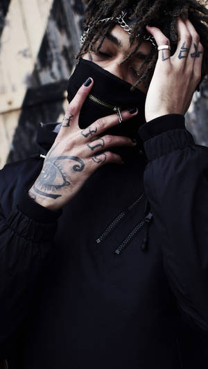有辮子頭和刺青的人在城市環境中調整黑色口罩。 — Scarlxrd 壁紙
