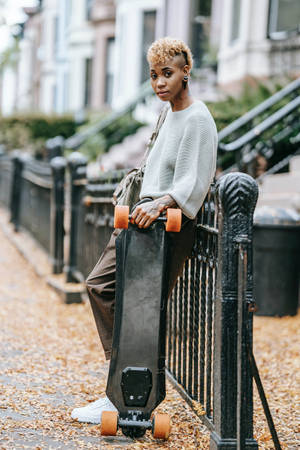 人靠在圍欄上，在鋪滿秋葉的人行道上拿著長板。 — 滑板 GIF 壁紙