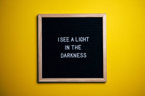 黃色牆上帶有訊息 I SEE A LIGHT IN THE DARKNESS 的字母板 — 正向 壁紙