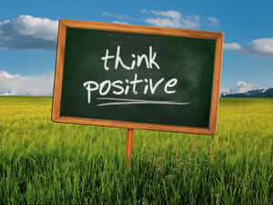 草地中的黑板，藍天下有 think positive 訊息 — 正向 壁紙