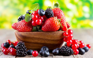 一個木碗裝滿各種新鮮莓果，放在木質表面上。 — 莓果 壁紙