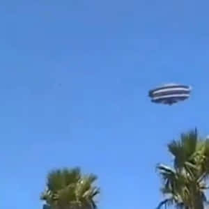 一個條紋UFO在藍天下的棕櫚樹上空飛行。 — 太空船 壁紙