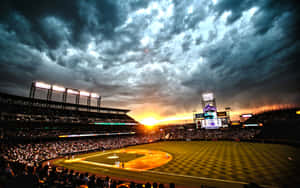 棒球場在日落比賽期間擠滿球迷，上方是戲劇性的雲層。 — 酷棒球 壁紙