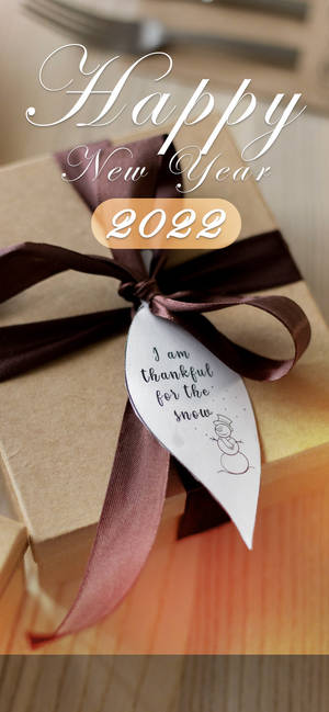 一個帶有雪人標籤的禮物盒，標籤上寫著「I am thankful for the snow」，用於2022年新年。 — iPhone 15 壁紙