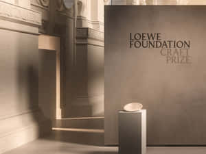 一個陶瓷碗放在陽光照射的畫廊基座上，牆上寫有「Loewe Foundation Craft Prize」文字。 — 慶祝 壁紙