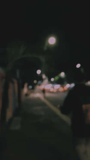 一個人在夜晚走在黑暗的城市人行道上，有模糊的路燈和交通。 — 城市 壁紙