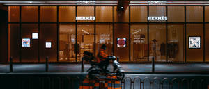 一輛機車在夜間經過愛馬仕商店，帶有發光的橙色燈光。 — 改裝摩托車 壁紙