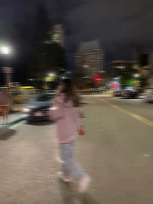 一個穿著粉紅色連帽衫的人，在夜晚的城市街道上行走，帶有模糊的動作和發光的車燈。 — 道路 壁紙
