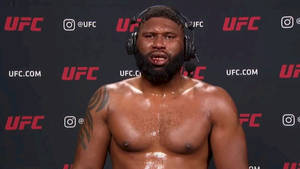 赤裸上身的UFC拳手，戴著耳機和鬍子，站在品牌牆前。 — 終極格鬥冠軍賽 壁紙