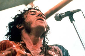汗流浹背的搖滾音樂家在舞台上熱情地對著麥克風唱歌。 — Woodstock 壁紙