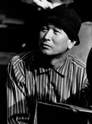 一個戴著帽子和條紋襯衫的男人在攝影棚裡若有所思地看向鏡頭外。 — 黒死牟 壁紙