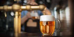一個冰涼的啤酒杯帶有泡沫，放在有金色龍頭和調酒師的吧檯上。 — 啤酒 壁紙