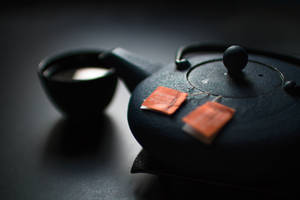 深色茶壺和杯子，帶橙色茶包，置於陰影表面。 — 日式 壁紙