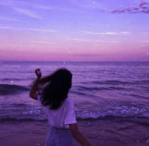 深色頭髮的人站在沙灘上面向海洋，背景是紫色日落。 — 海灘 壁紙