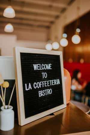 咖啡店內一個木框字母板寫著「Welcome to La Coffeeteria Bistro」，旁邊有一個白色花瓶。 — Huawei MatePad 壁紙