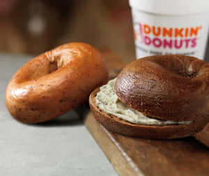 烤百吉餅配奶油乳酪和Dunkin' Donuts咖啡杯在木板上。