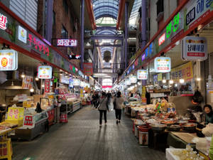 購物者穿過一個熱鬧的室內韓國市場，市場內有發光的招牌和美食攤位。