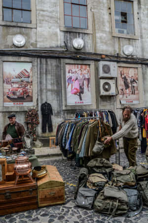復古服裝和袋子陳列在鵝卵石街道上，混凝土牆上有復古海報。 — 小米平板 8 Pro 壁紙