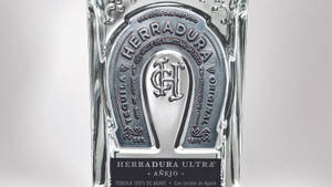Herradura Ultra Añejo 龍舌蘭酒瓶的特寫，帶有銀色馬蹄鐵標誌。 — 酷 壁紙