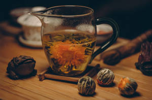 玻璃壺中盛開的菊花茶，木桌上放有青蛙公仔和茶球。 — 派對 壁紙