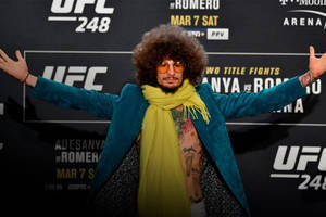 UFC活動中留爆炸頭戴太陽眼鏡的男人，身穿藍綠色外套和黃色圍巾。 — 終極格鬥冠軍賽 壁紙